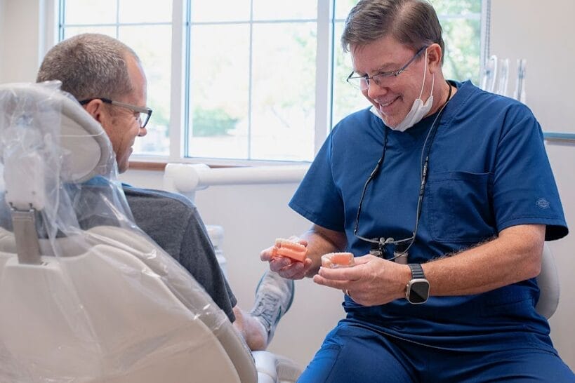 Dentist holding dentures while consulting a patient in a dental chair